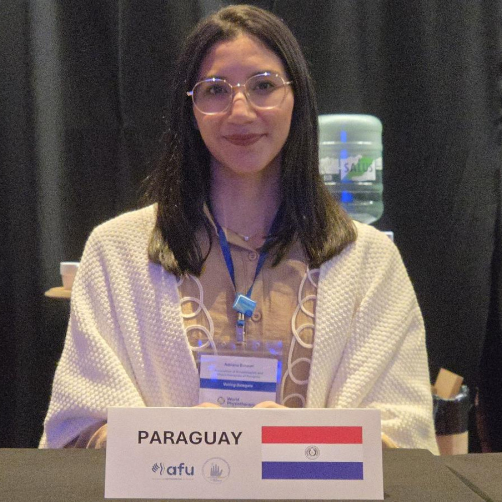 A young female professional in a white coat sat behind a meeting desk with a card saying Paraguay
